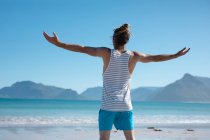 Rear view of man standing with arms outstretched while looking towards sea against blue sky. recreation and nature. — Stock Photo