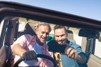 Felice caucasico gay maschio coppia prendere selfie seduto in auto al mare. estate viaggio su strada e vacanza nella natura. — Foto stock