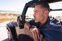 Thoughtful caucasian man sitting in car at seaside admiring the view. summer road trip and holiday in nature. — Stock Photo