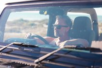 Thoughtful caucasian man wearing sunglasses sitting in car on sunny day at seaside. summer road trip and holiday in nature. — Stock Photo