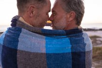 Felice caucasico gay coppia maschile avvolto in coperta, abbracciando e prendendo selfie sulla spiaggia al tramonto. estate viaggio su strada e vacanza nella natura. — Foto stock