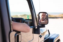 Ritratto di uomo caucasico sorridente in auto riflesso nello specchio laterale nella giornata di sole al mare. estate viaggio su strada e vacanza nella natura. — Foto stock