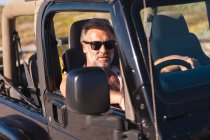 Retrato de homem caucasiano usando óculos de sol sentado no carro no dia ensolarado à beira-mar. viagem de verão e férias na natureza. — Fotografia de Stock