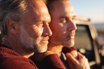 Happy caucasian gay male couple embracing in sun, enjoying the view at seaside. summer road trip and holiday in nature. — Stock Photo