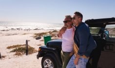 Happy caucasian gay male couple embracing and enjoying the view by car at seaside. summer road trip and holiday in nature. — Stock Photo