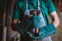 Ein Schmied in Schutzkleidung hält den Hammer in der Hand, während er in der Industrie steht. Schmiede-, Metall- und Fertigungsindustrie. — Stockfoto
