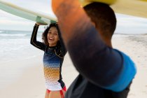 Amigas multirraciais felizes carregando pranchas de surf na cabeça na praia durante o fim de semana. amizade, surf e lazer. — Fotografia de Stock