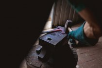 Immagine ritagliata di fabbro in guanti protettivi forgiatura con martello su incudine nell'industria. forgiatura, lavorazione dei metalli e industria manifatturiera. — Foto stock