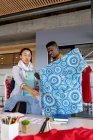 Diseñadores de moda multiraciales masculinos y femeninos discutiendo sobre tela estampada azul en la oficina. negocio de diseño creativo, oficina moderna y moda. - foto de stock