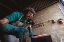 Bearded caucasian blacksmith in protective workwear forging with hammer on anvil in industry. forging, metalwork and manufacturing industry. — Stock Photo