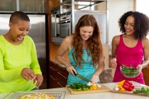 Fröhliche multiethnische junge Freundinnen in Kasualien, die zu Hause in der Küche gemeinsam Pizza zubereiten. Freundschaft, Geselligkeit, Kochen und Hausfest. — Stockfoto
