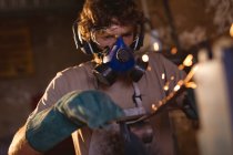 Caucasian blacksmith wearing gas mask while working on metal in industry. forging, metalwork and manufacturing industry. — Stock Photo