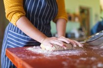 Eine Frau mit Schürze knetet Teig auf einem Holztisch in der heimischen Küche. Lebensstil und gesunde Ernährung. — Stockfoto