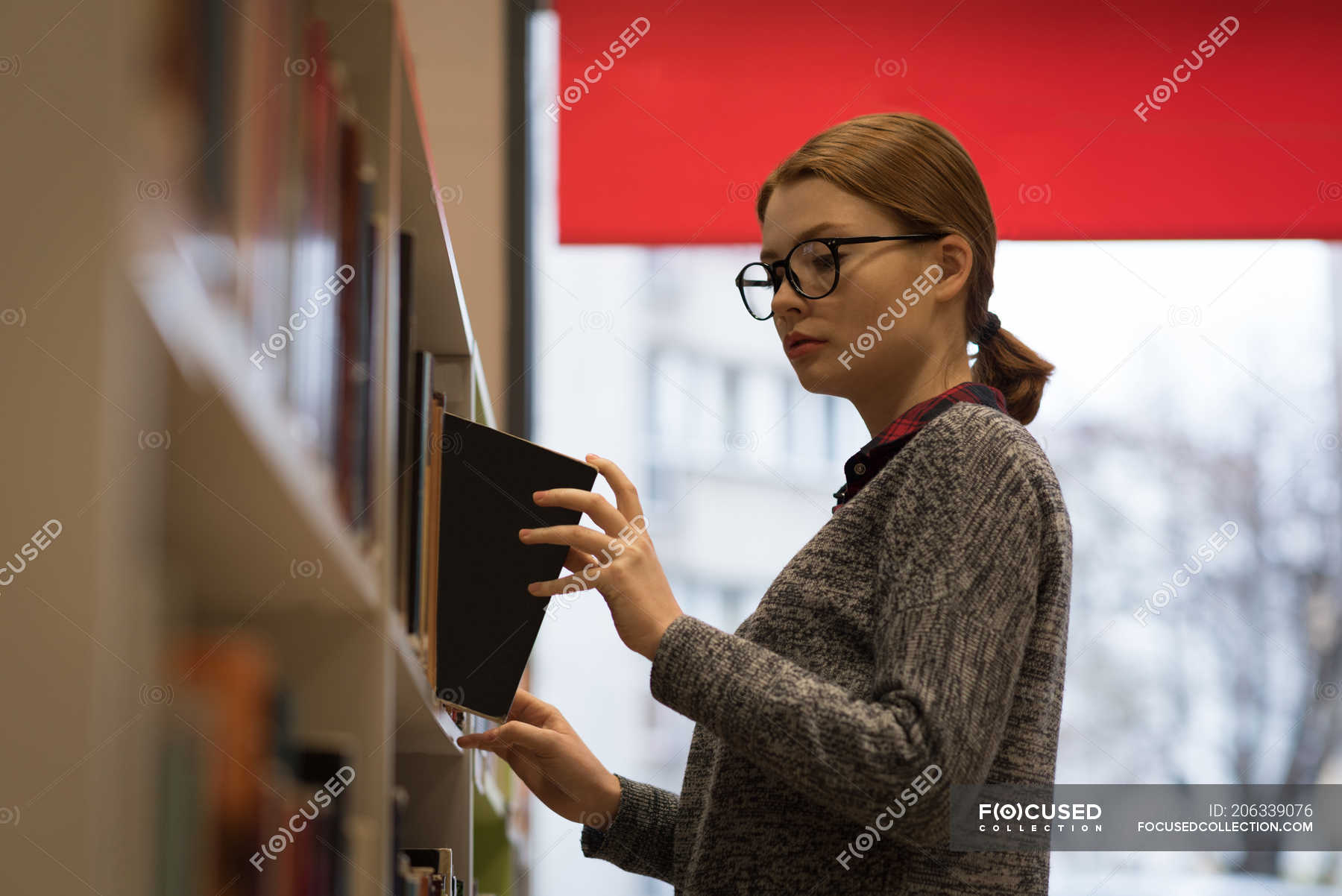 Young woman picking up a book from the bookshelf — choice, studying ...