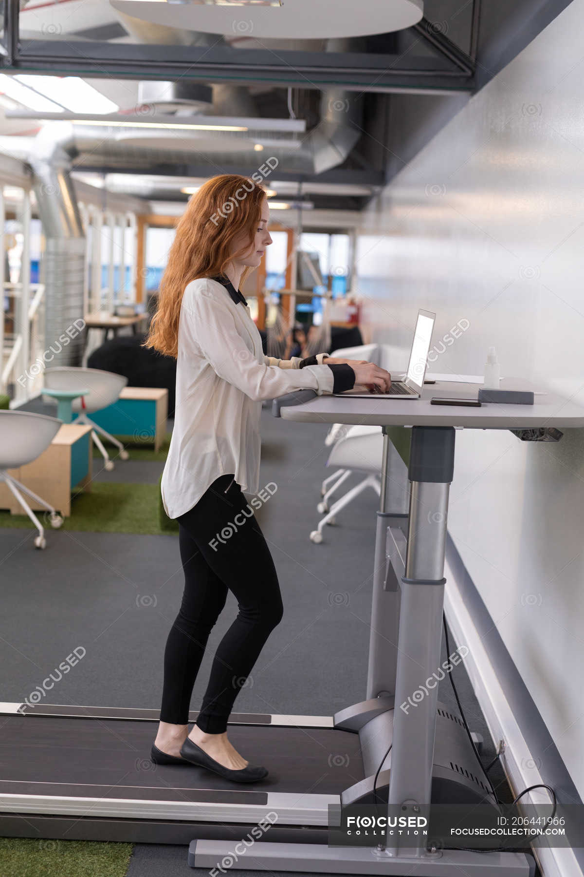 Female Executive Using Laptop While Exercising On Treadmill In
