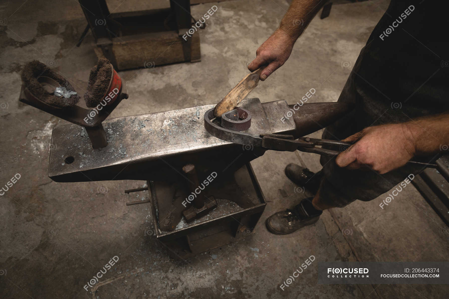 Blacksmith using hand wire brush on metal rod in workshop — industry