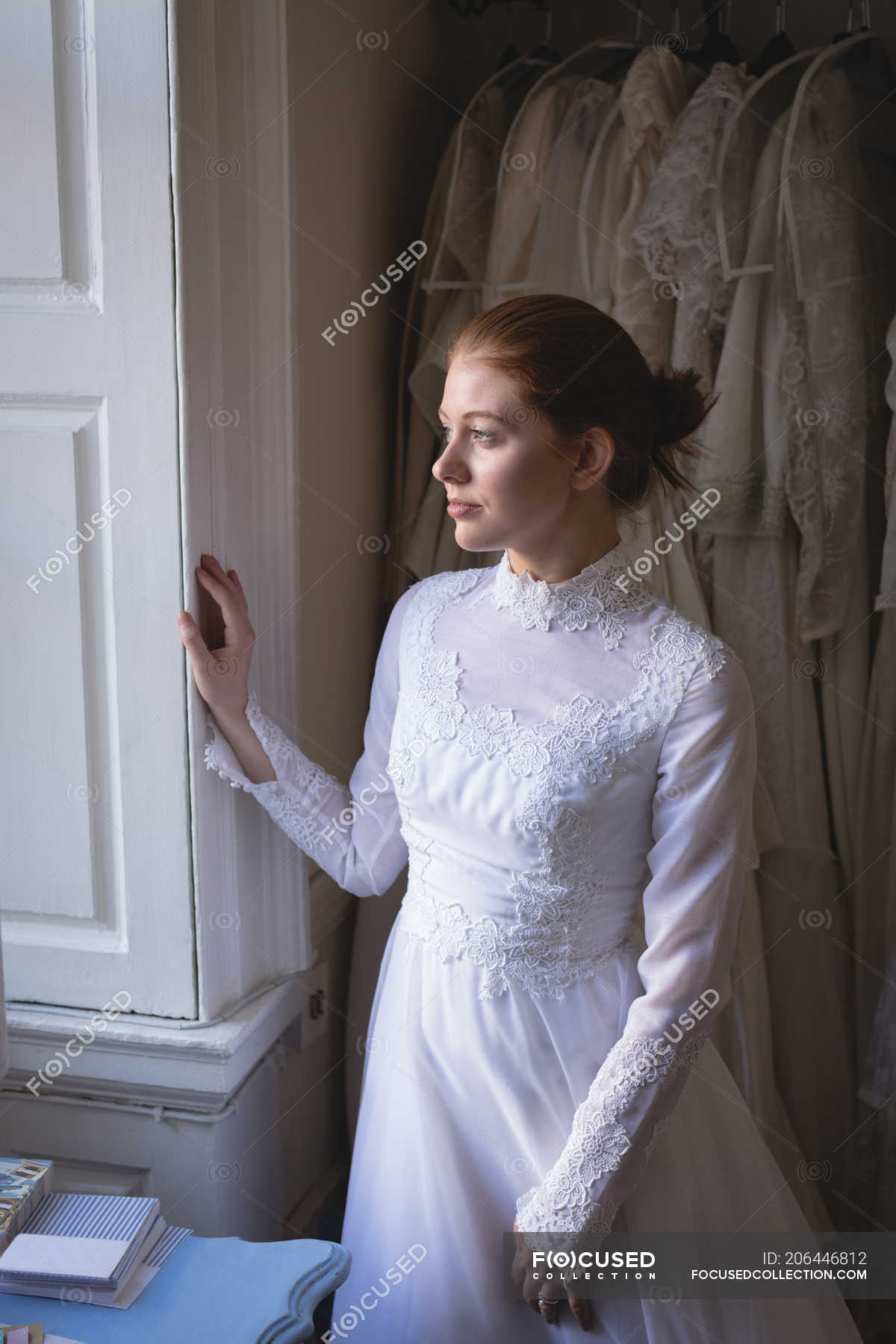 Red hair bride white dress looking through the window at boutique — fashionable, - Stock Photo #206446812