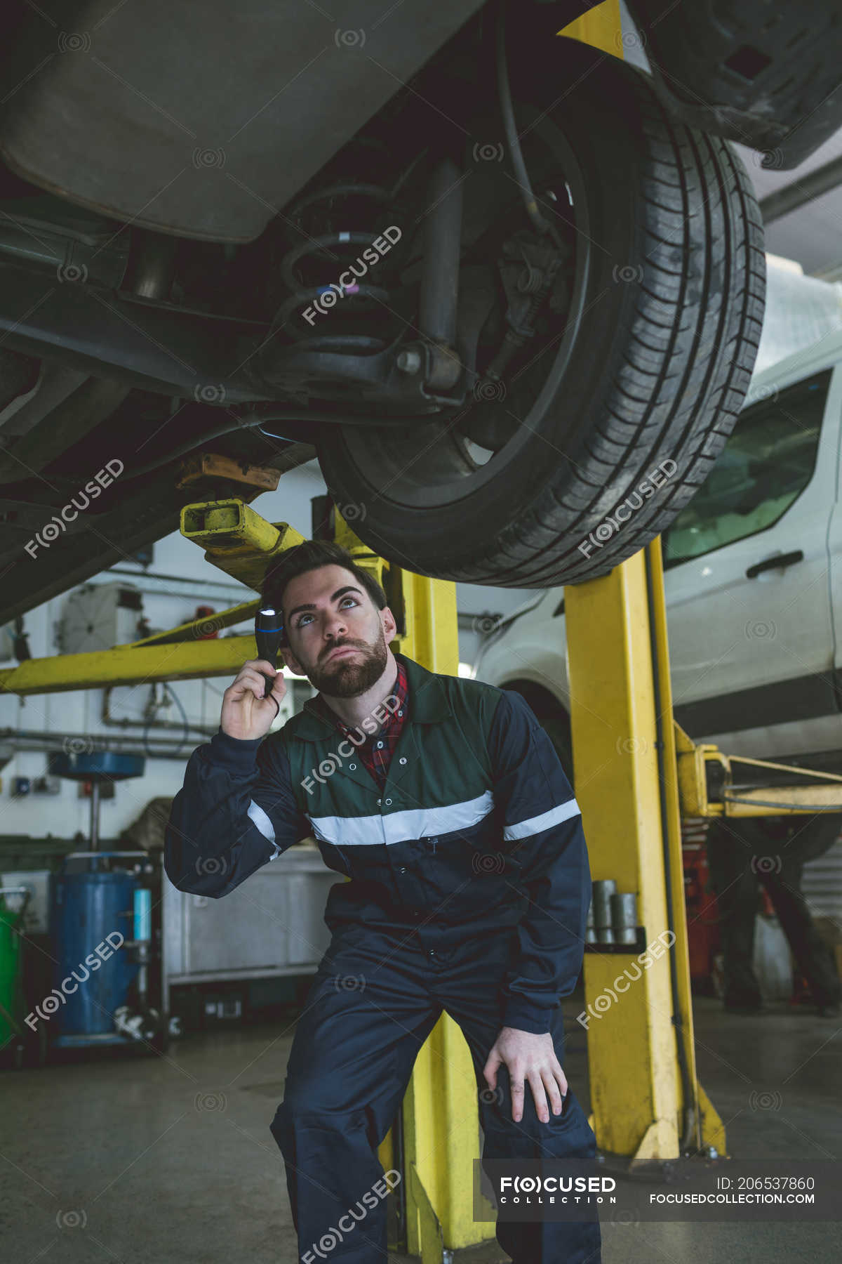 Male mechanic examining a car with torch in repair garage — Auto Repair ...