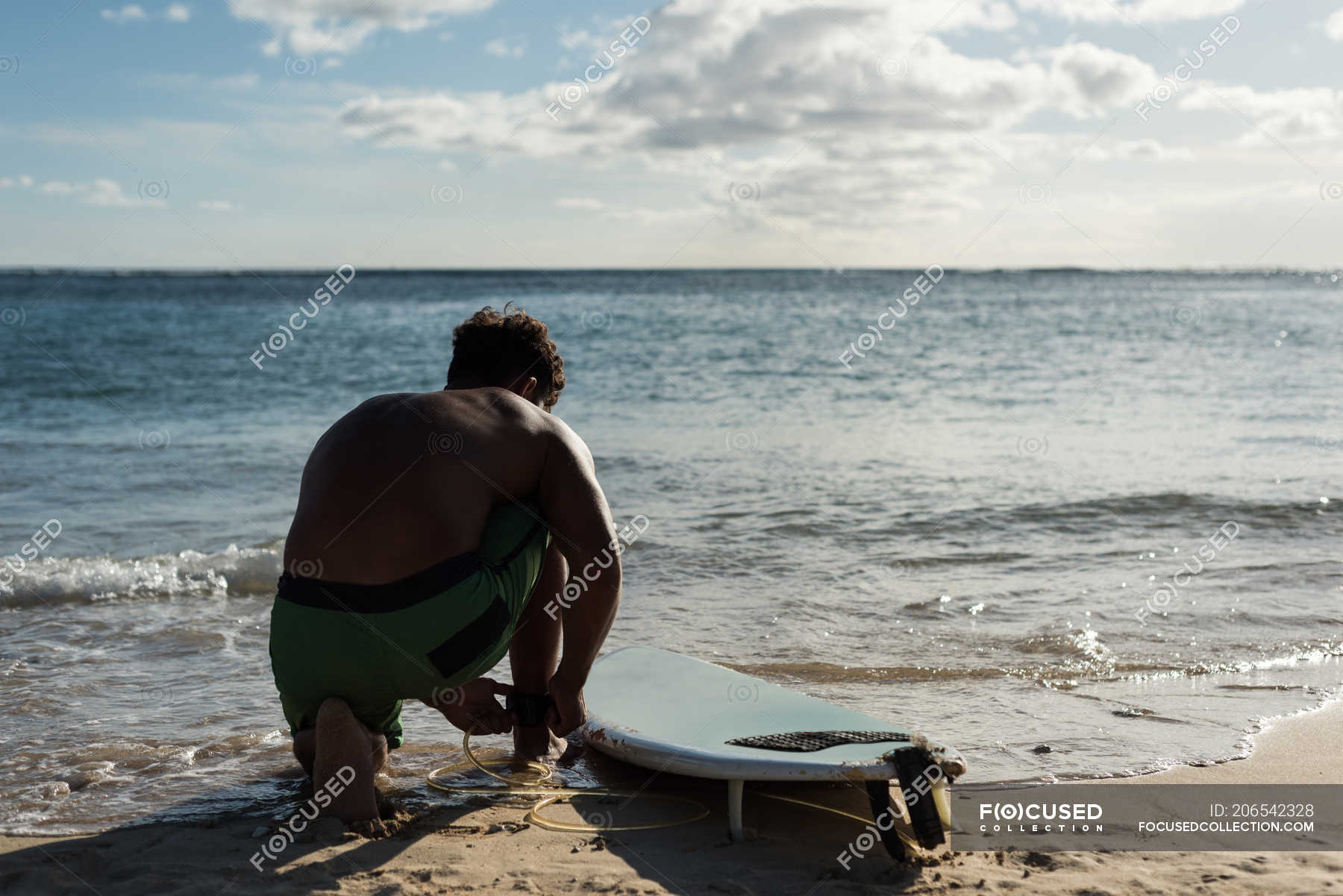 Male surfer tying surfboard leash on his leg at beach — sunny, modern ...