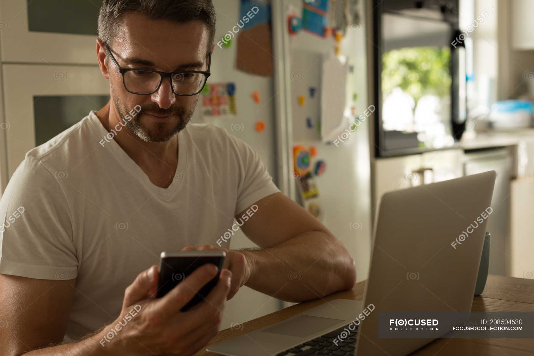 Man using mobile phone while working on laptop at home — notebook ...