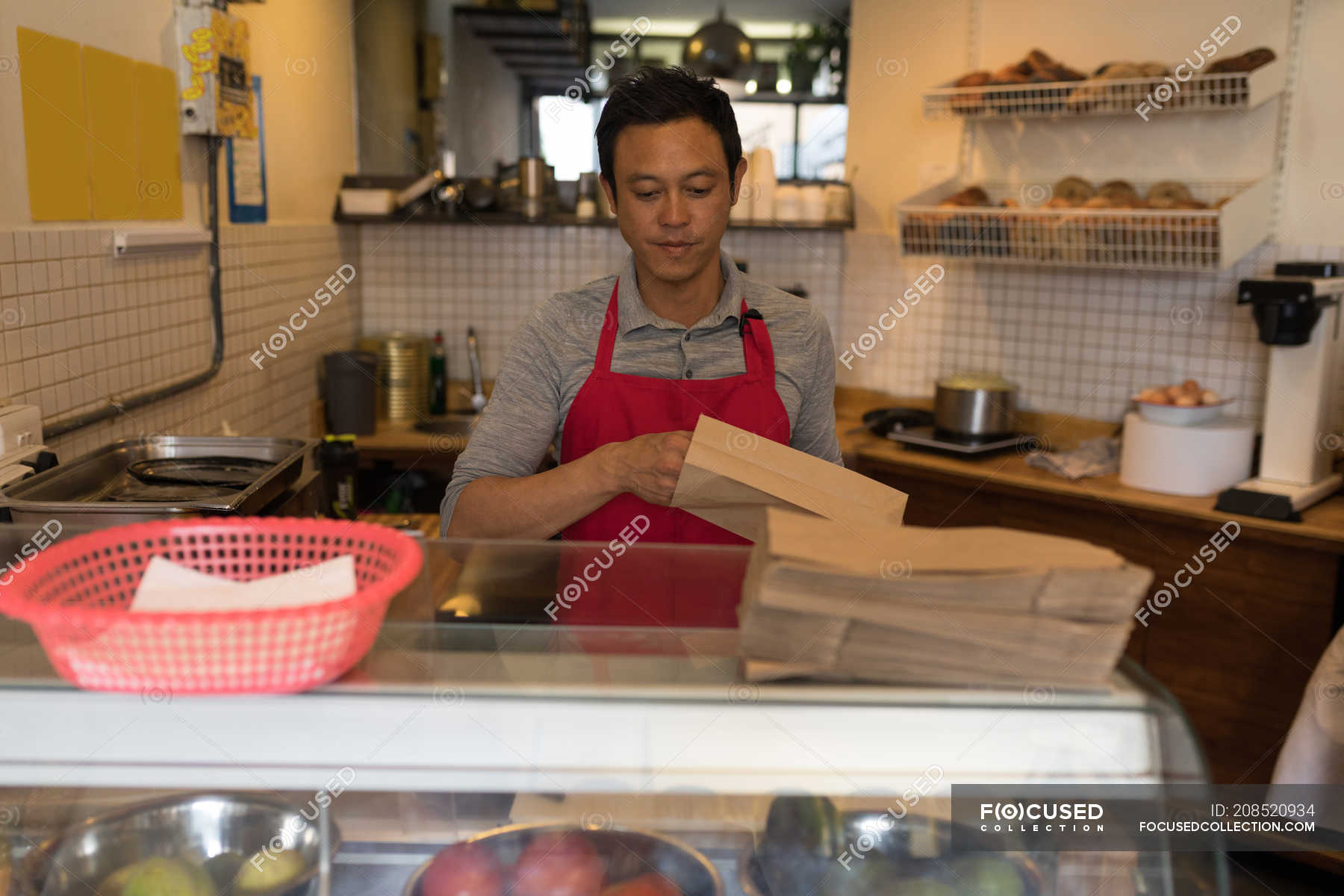 Male Staff Packing Food In Paper Bag In Coffee Shop Standing