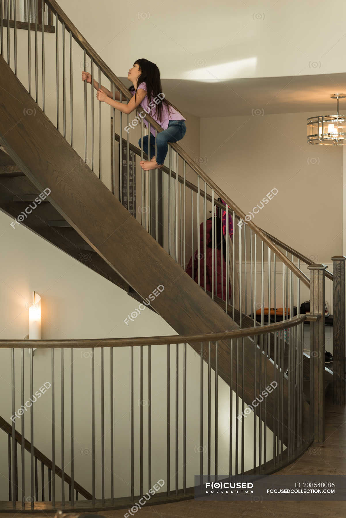 Happy girl playing on staircase railing at home — self isolation ...