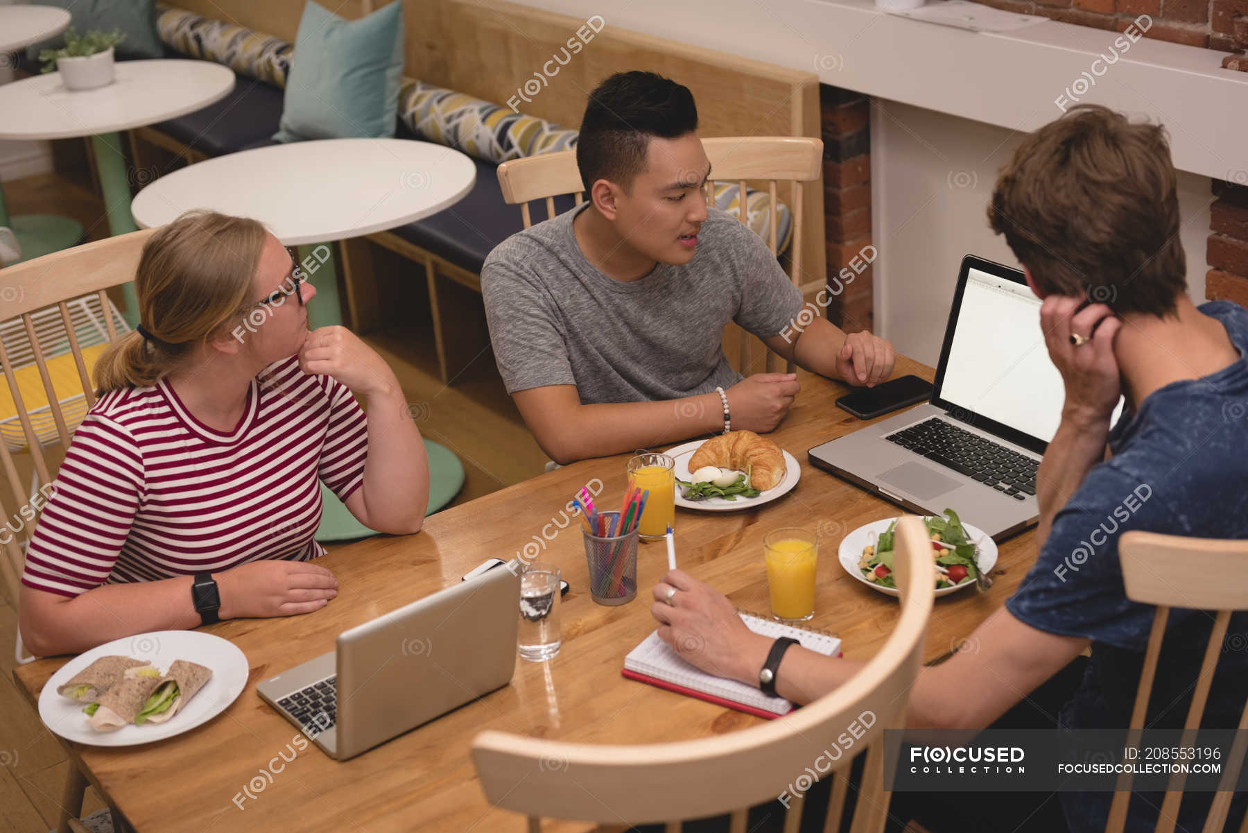 Executives discussing over laptop with each other in the cafeteria at ...