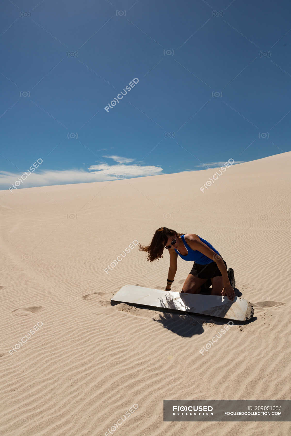 Woman applying surfboard wax to sandboard at desert on a sunny day