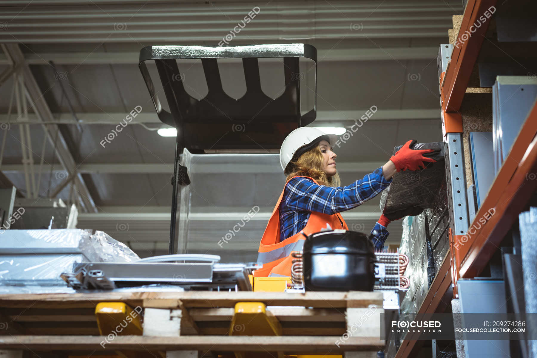 Female worker unloading machine part from rack in factory — copy space ...