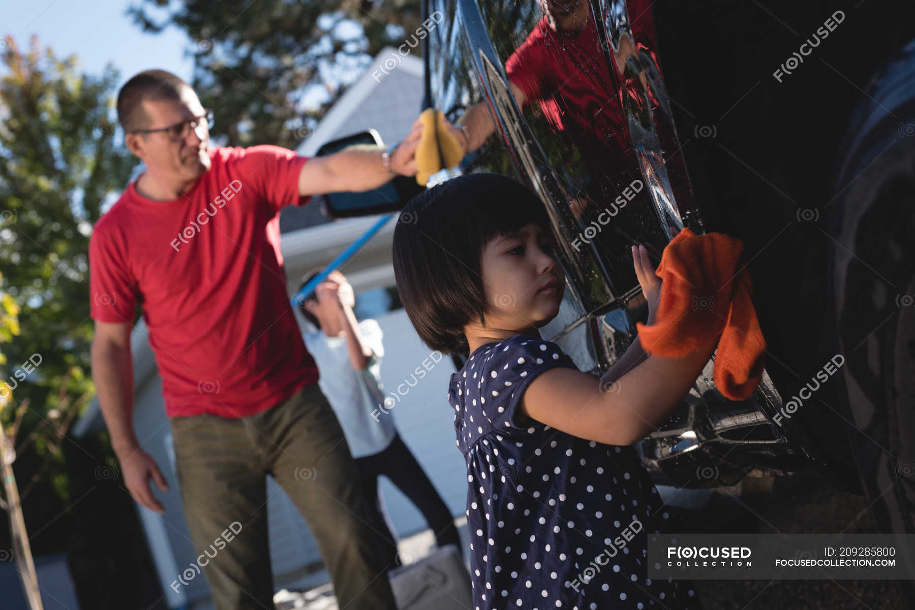 father-and-daughter-washing-car-with-sponge-and-duster-outside-garage