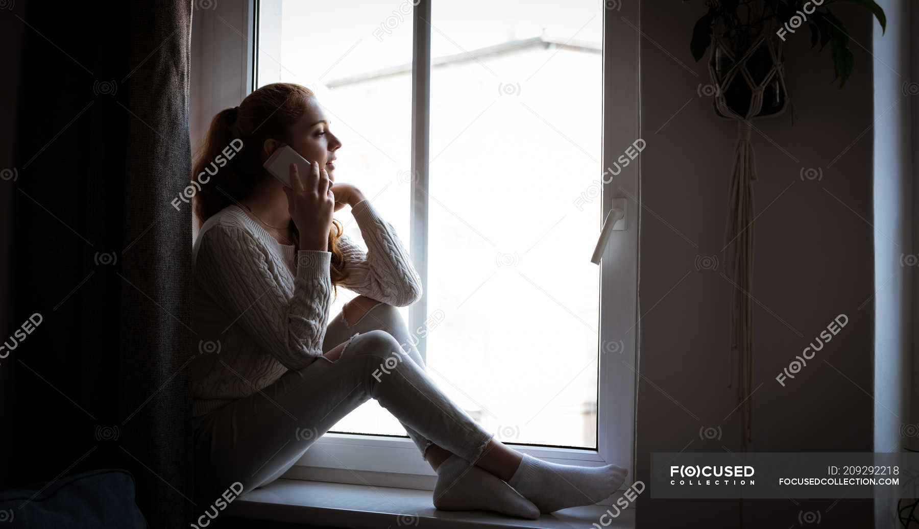 Teenage Girl Sitting On Window Sill And Talking On Mobile Phone At Home 6673