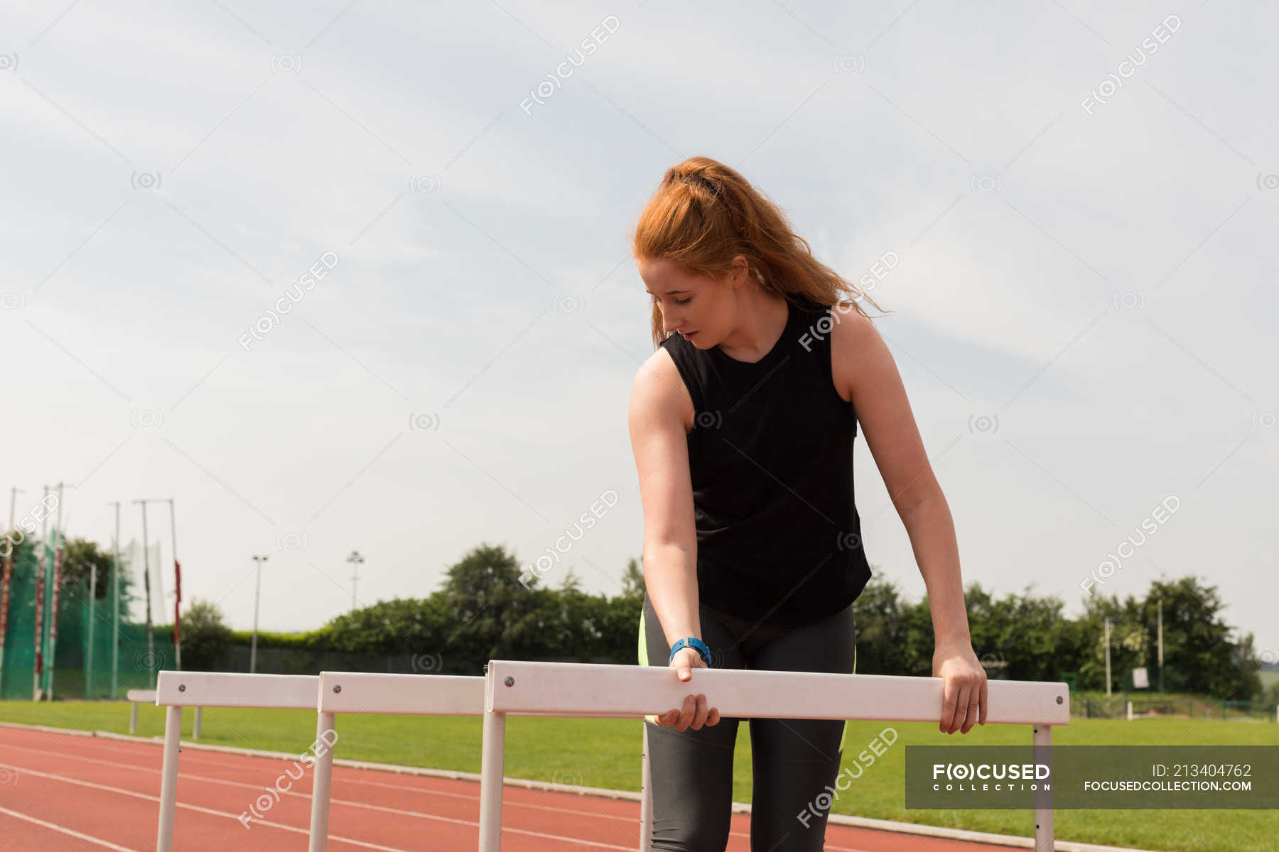 Young female athlete arranging hurdles on running track — markings