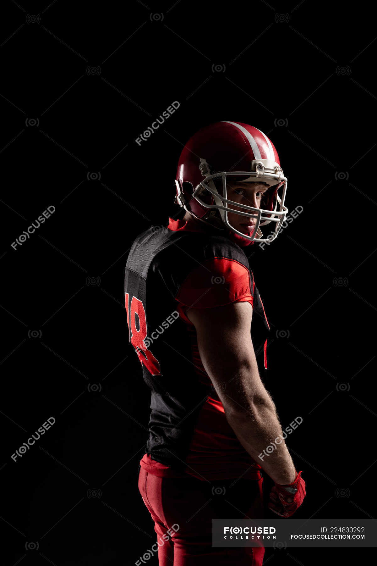 Young American football player in helmet standing against black ...