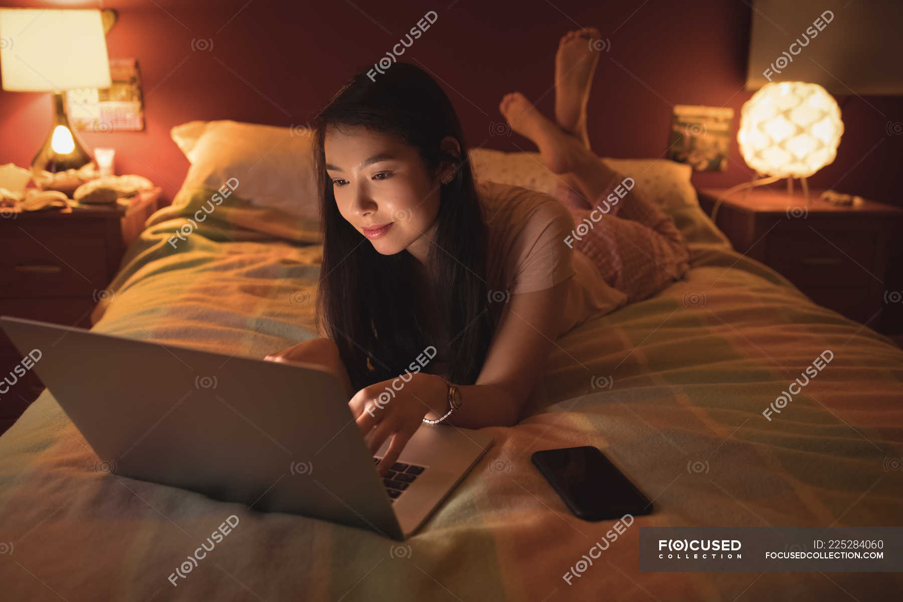 Woman lying and using laptop on bed in bedroom — indoors, interior Stock Photo 225284060