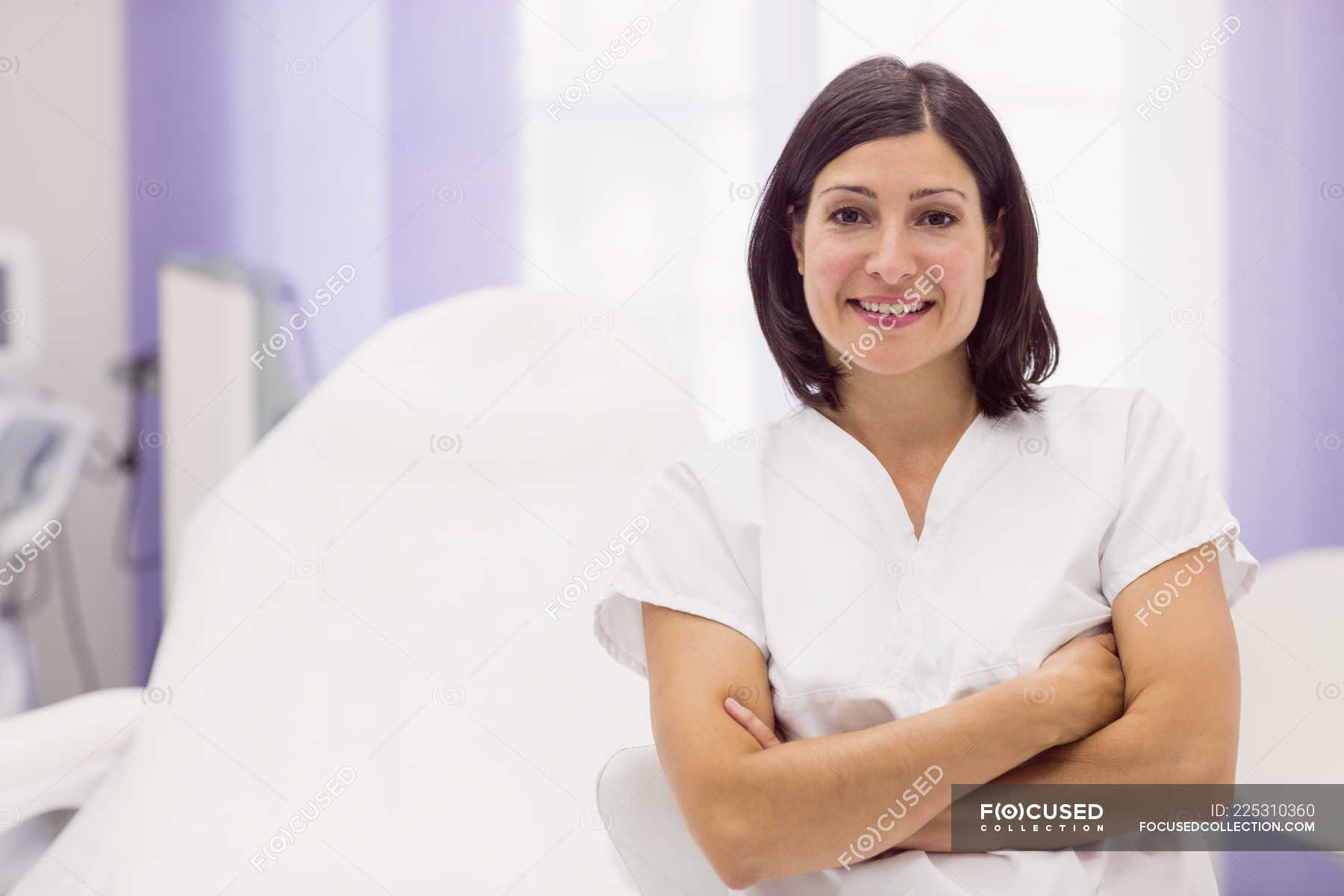 Portrait of female dermatologist standing with arms crossed in clinic ...