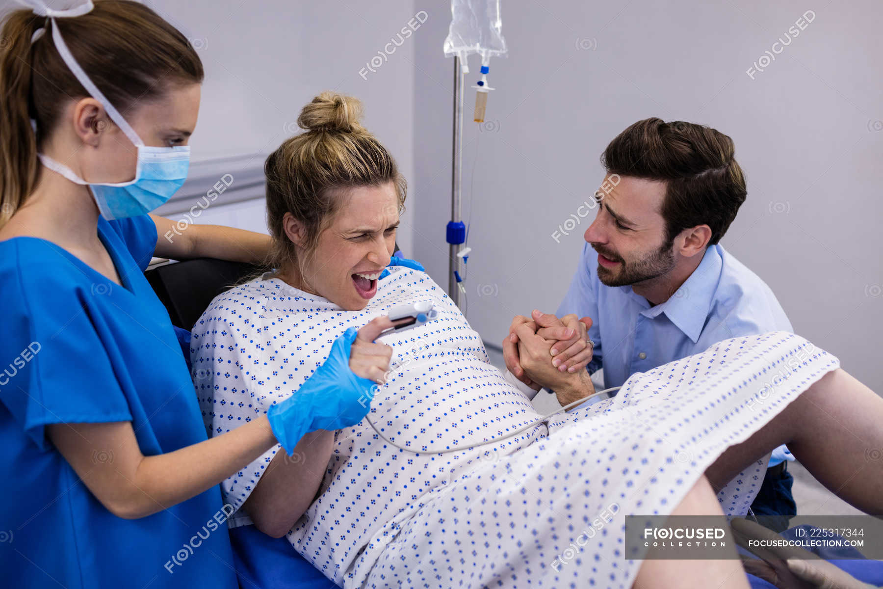 Doctor Examining Pregnant Woman During Delivery While Man Holding Her