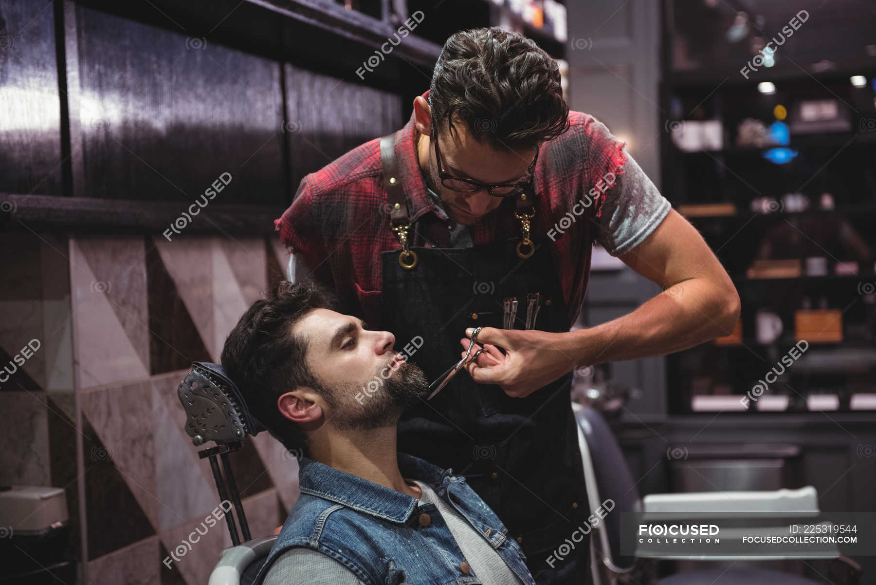 Man getting beard trimmed by barber with scissors in barber shop