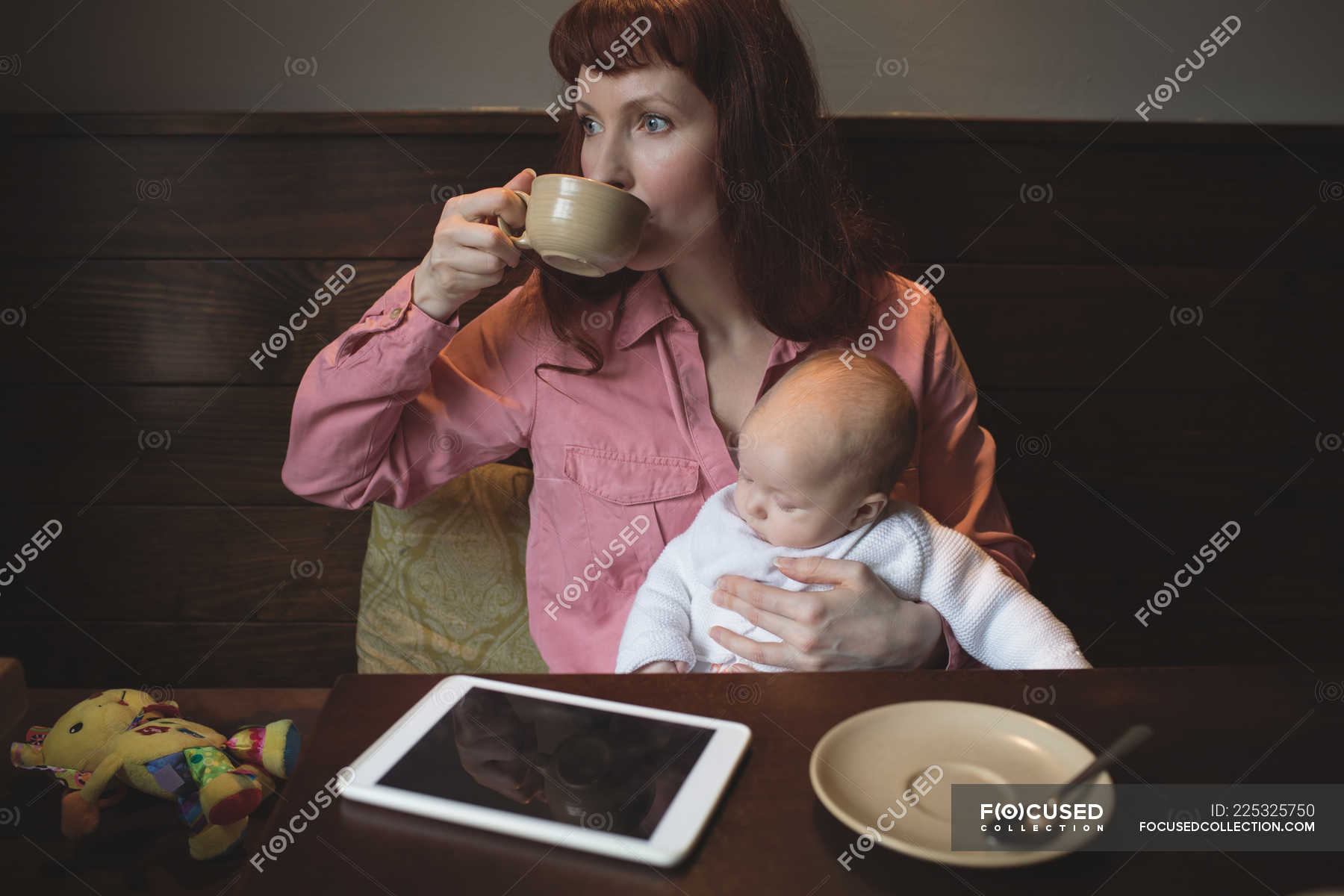 Mother having coffee while holding baby in coffee shop — sitting