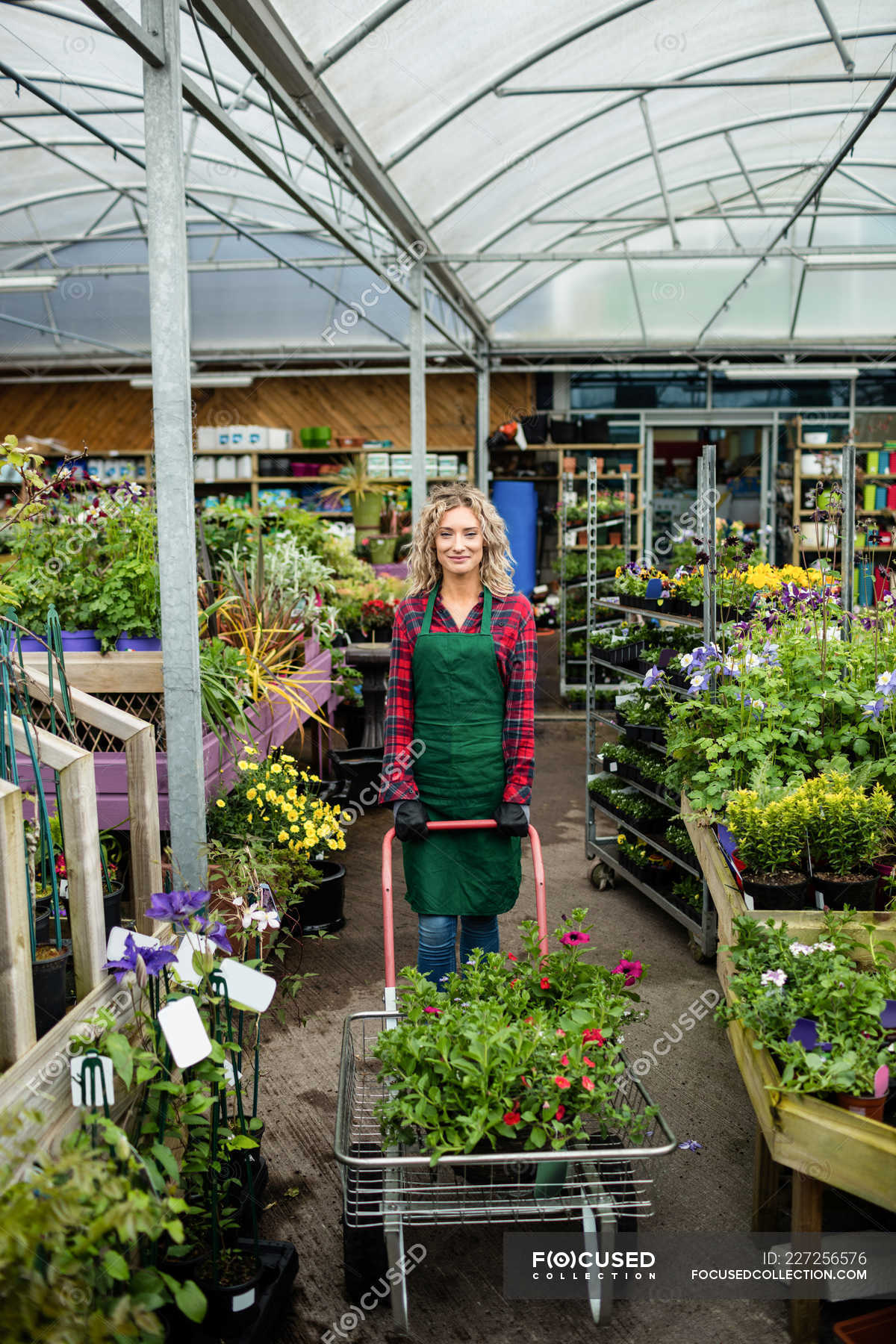 Portrait Of Female Florist Standing With Garden Trolley In Garden