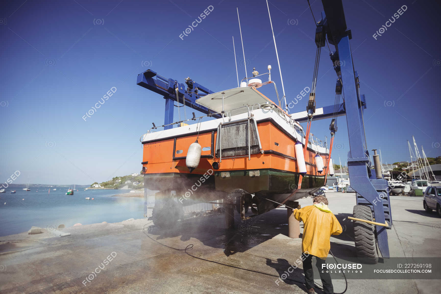 Man cleaning boat with pressure washer on sunny day — working