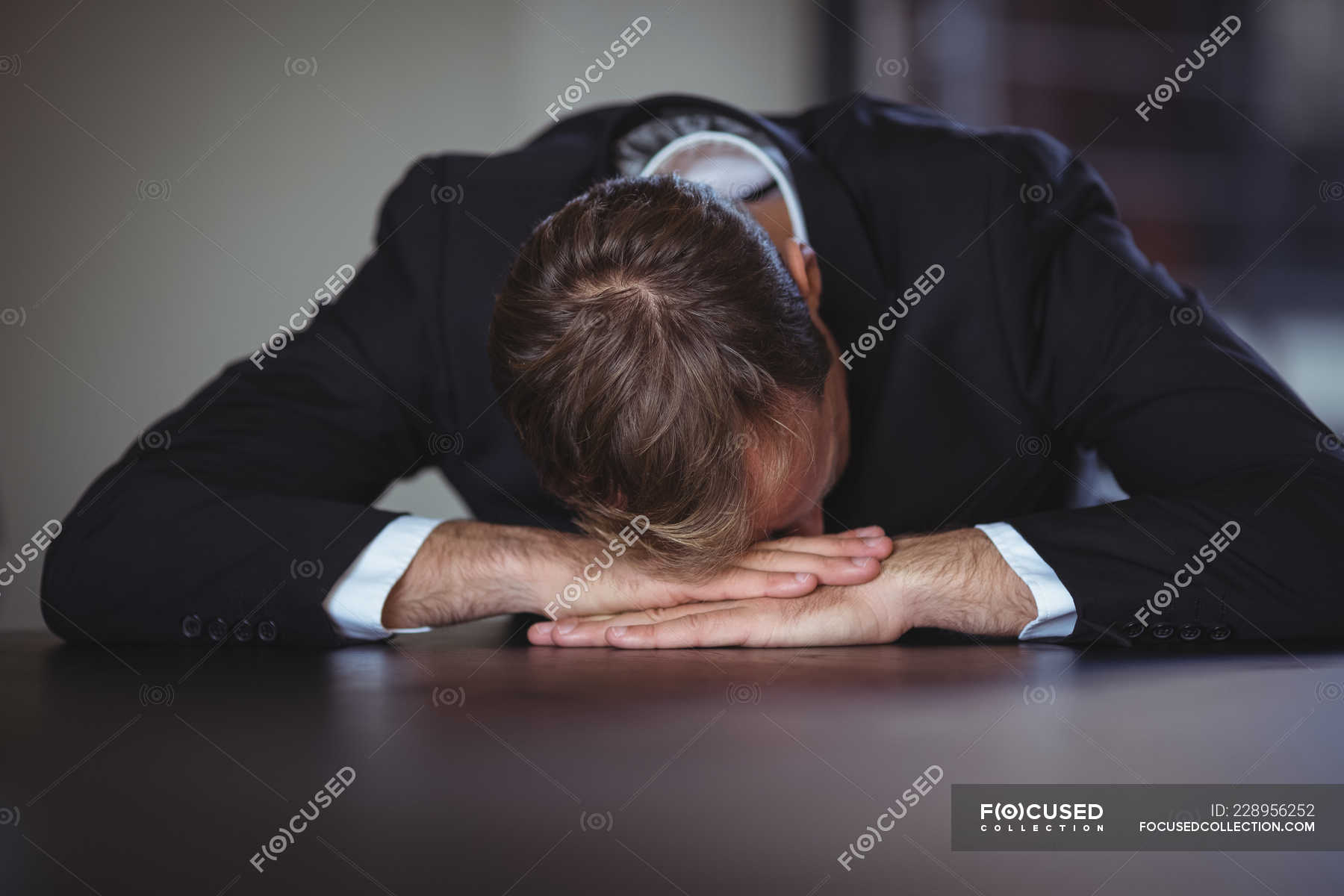Exhausted Businessman Sitting With His Head Down On Office Desk