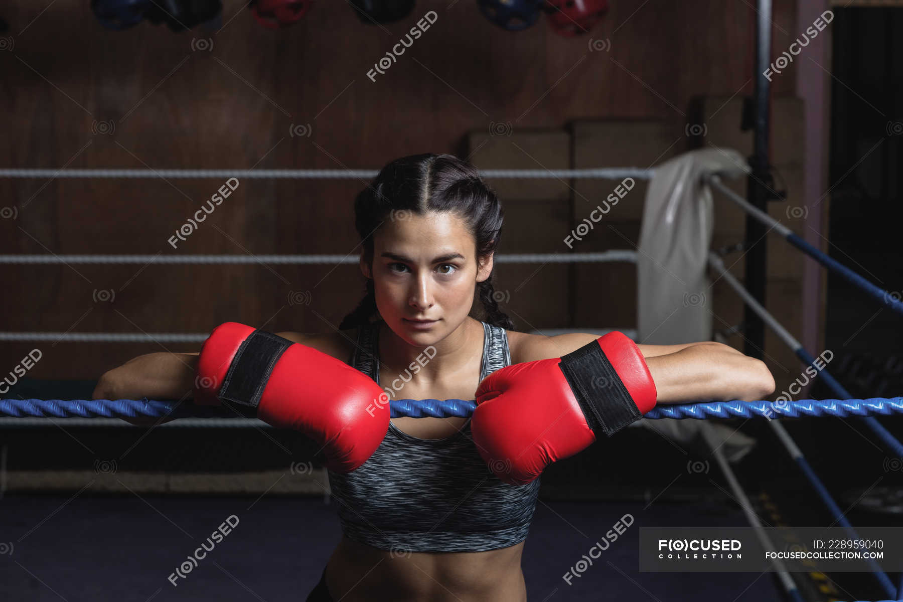 Tired female boxer in boxing gloves leaning on ropes of boxing ring at ...