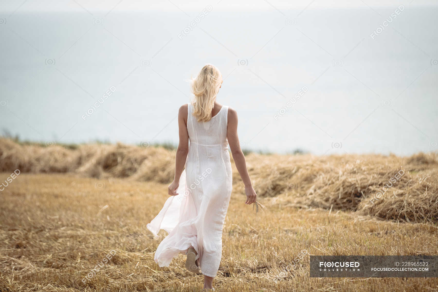 Back View Of Carefree Blonde Woman Walking In Field Near River — People
