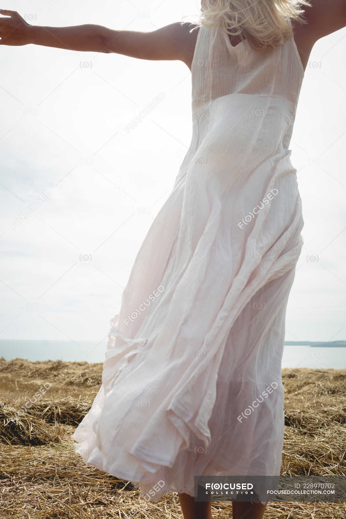 Rear View Of Carefree Blonde Woman In White Dress Standing On Field At