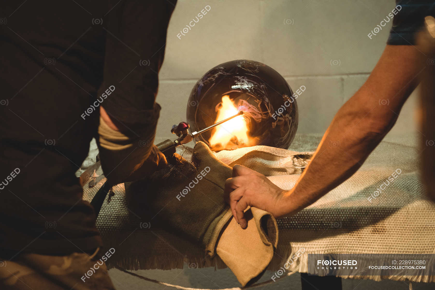 Team of glassblowers blowing propane gas flame on finished piece of