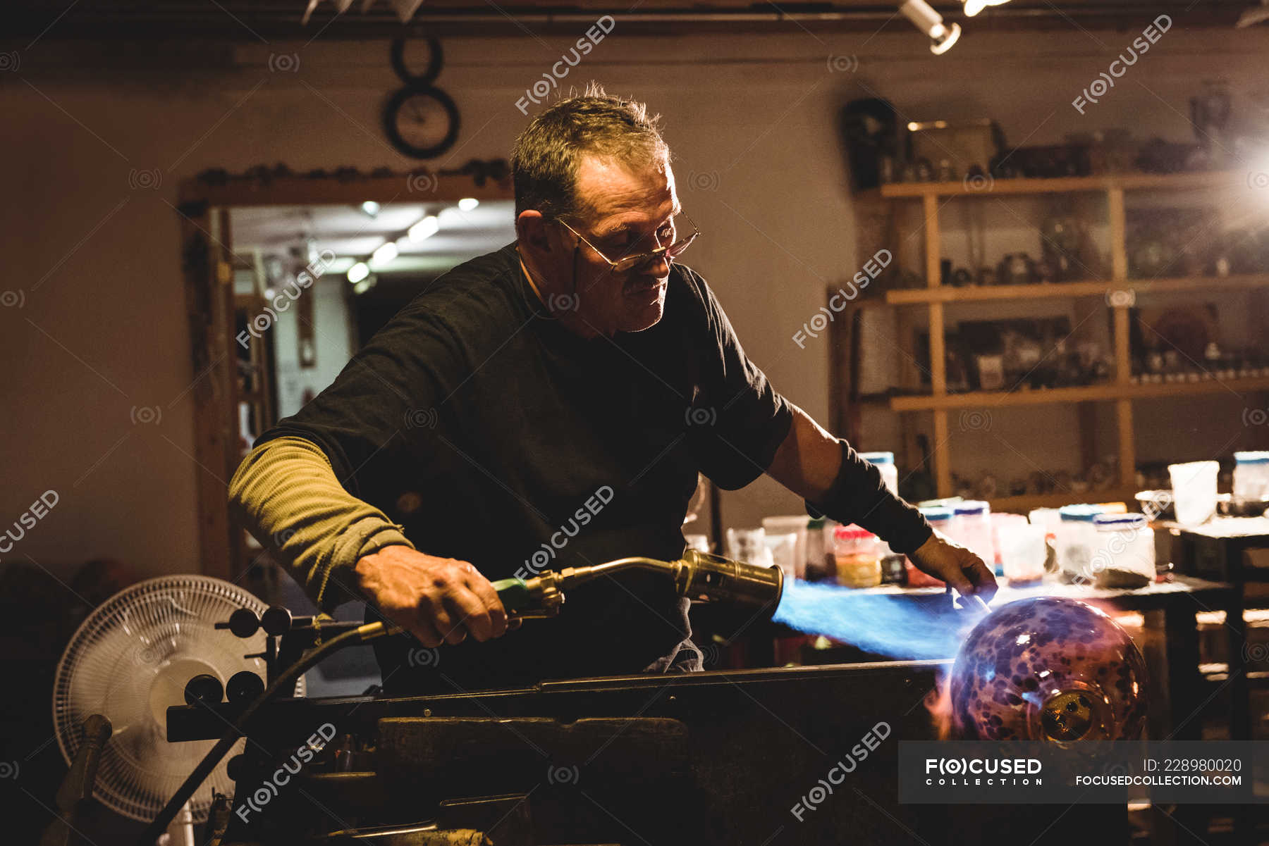 Glassblower blowing propane gas flame on finished piece of glass at