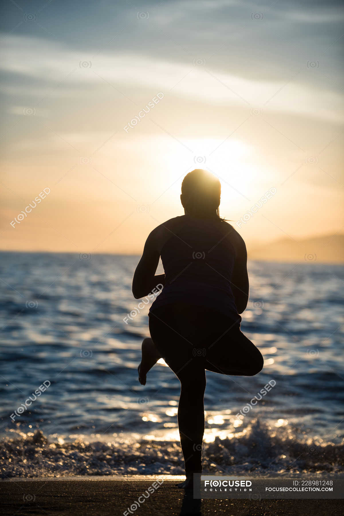 Back view of Woman performing yoga on beach during sunset — copy space ...