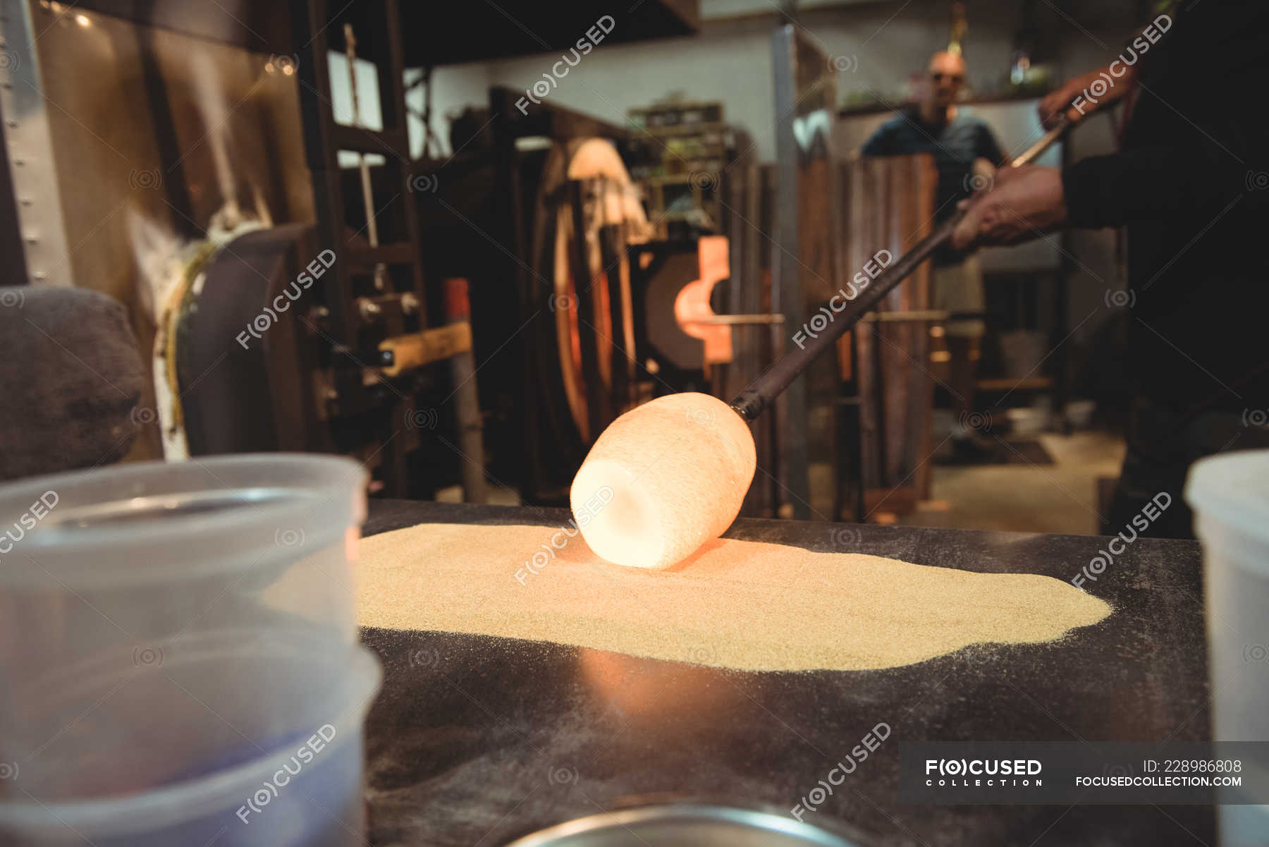 Glassblower rolling molten glass over blowpipe glass on table at ...