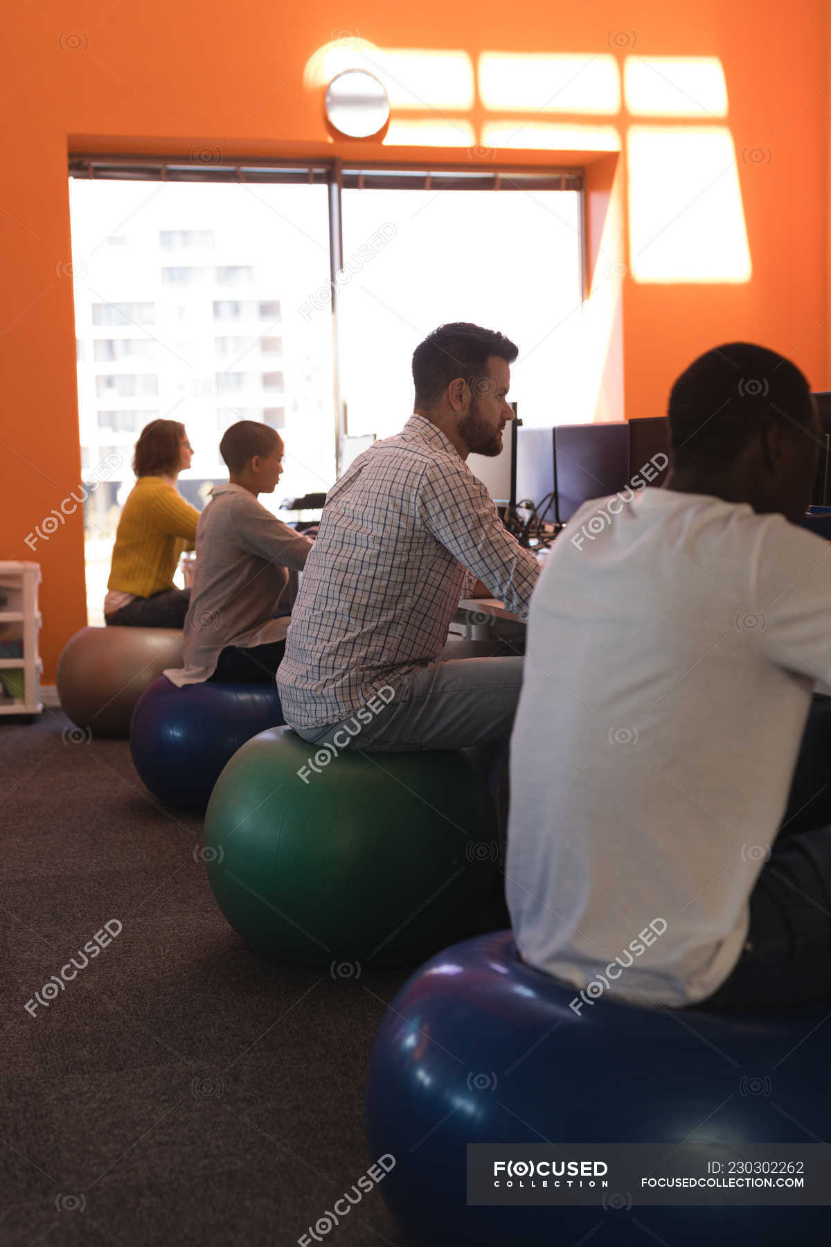 Business Executives Working At Desk While Sitting On Exercise Ball