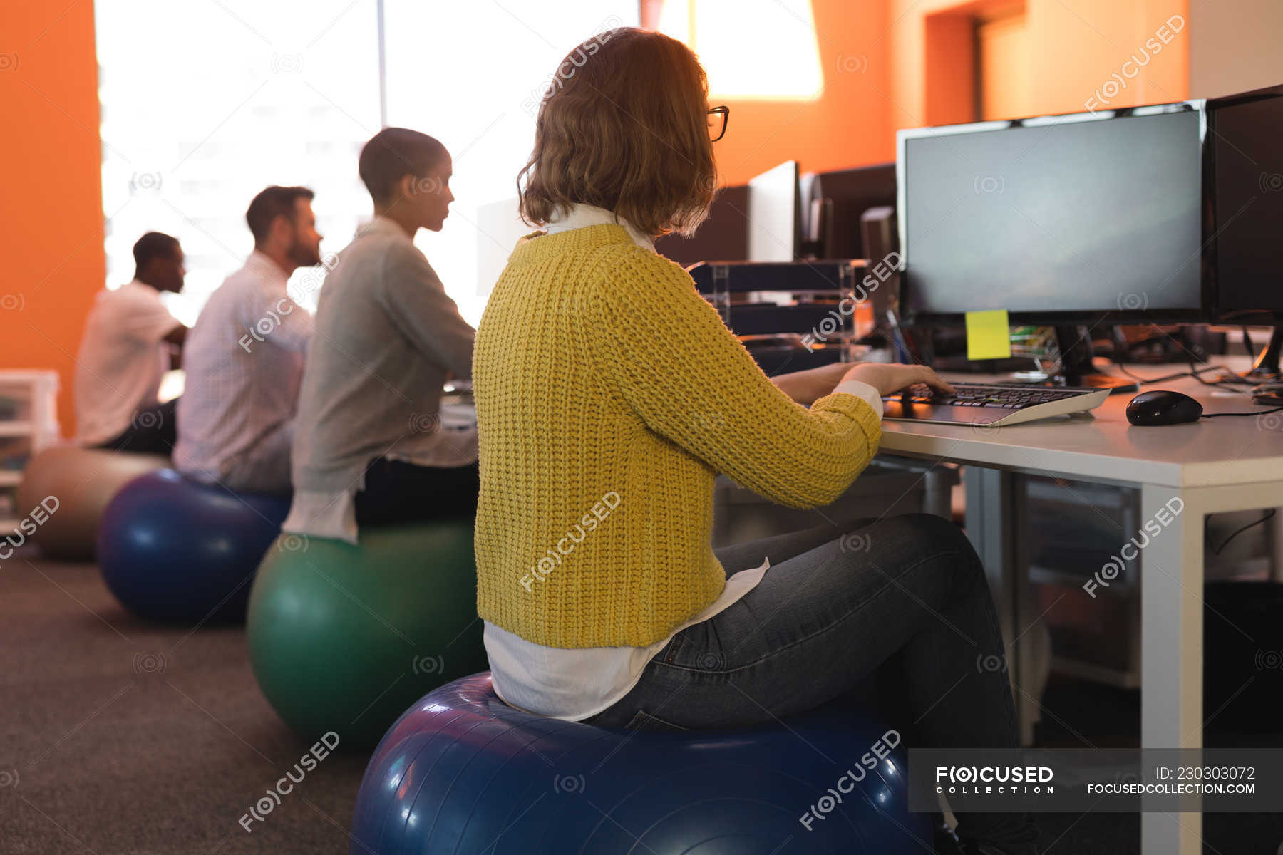 Business Executives Working At Desk While Sitting On Exercise Ball
